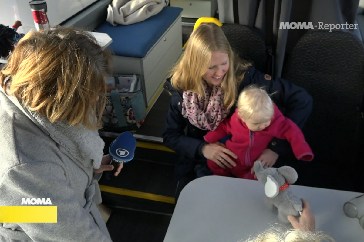 Die Reporterin interviewt eine Mutter mit Baby im Hebammenmobil. 